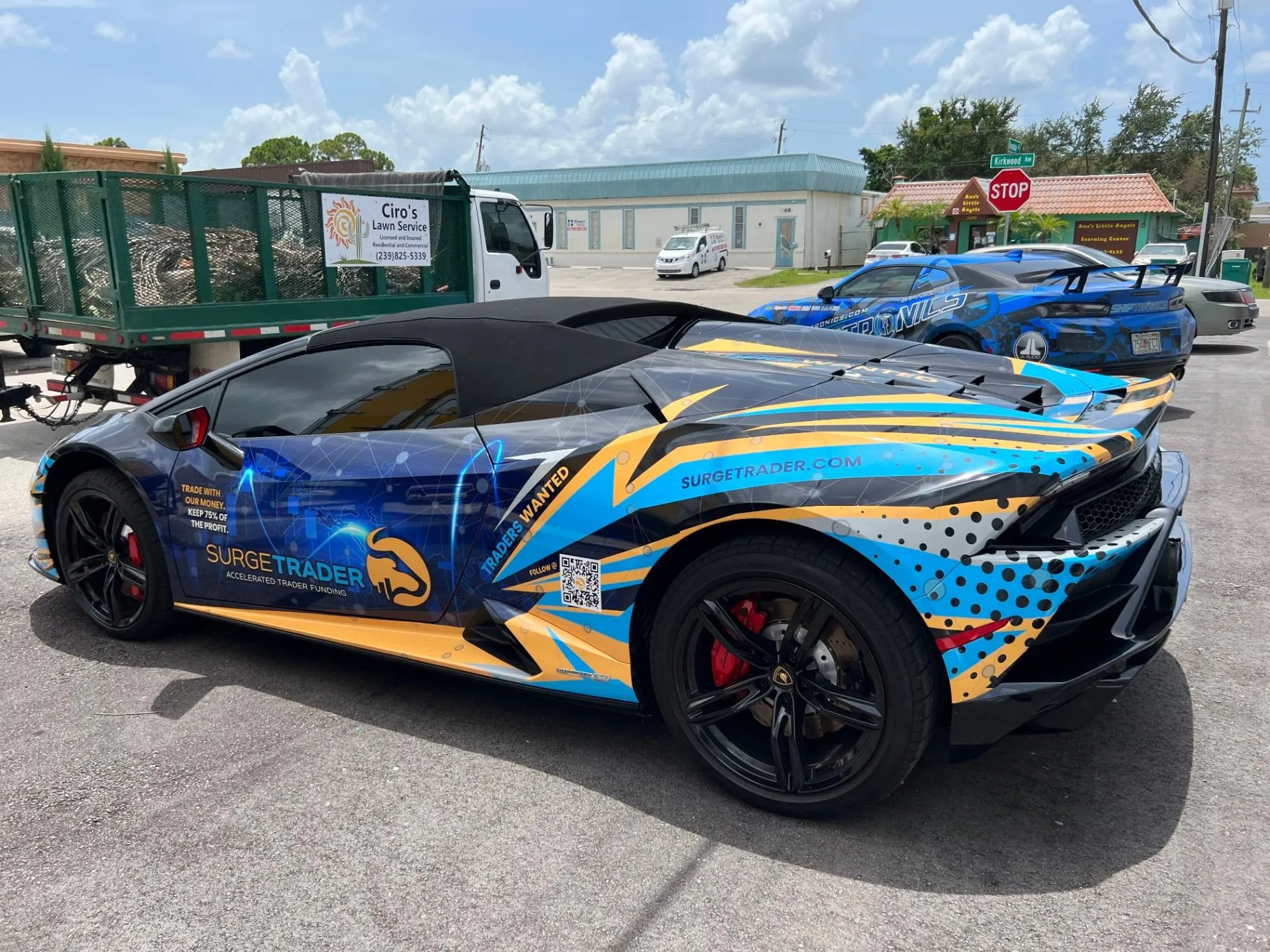 Blue and gold SurgeTrader-wrapped Lamborghini with a Shiptronics car in the background